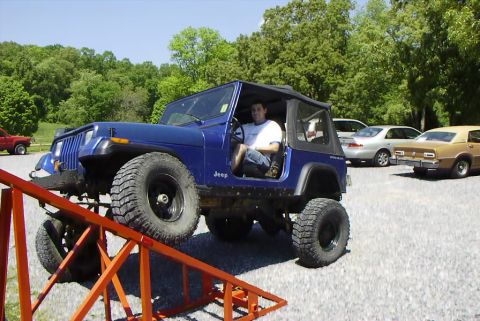 1995 Ford Bronco - A blue Jeep Wrangler is positioned on an orange ramp, with other vehicles parked in the background.