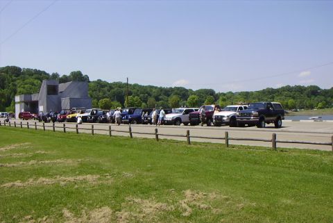 1995 Ford Bronco - A group of vehicles are parked in a lot near a body of water on a sunny day.