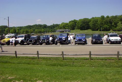 1995 Ford Bronco - A group of Jeeps and an SUV are parked in a line next to a lake on a sunny day.