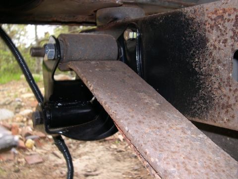 1994 Ford Bronco - Close-up of a rusty leaf spring and its mounting bracket, showing signs of wear and tear.