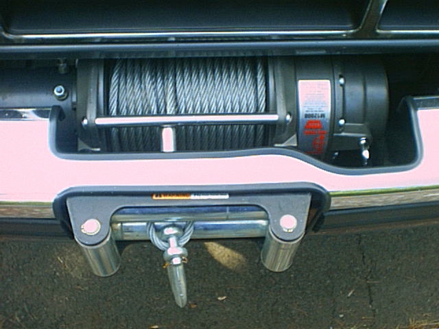 Winch with spooled steel cable and roller fairlead mounted behind a pink and chrome front bumper