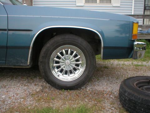 1987 Ford Crown Victoria LTD - A blue sedan's front fender and wheel are visible, with a spare tire lying nearby.