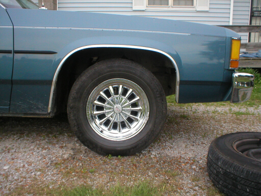 Blue sedan front fender and wheel with chrome trim, a spare tire is on the ground