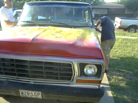1978 Ford Bronco - Front view of a 1978 Ford Bronco with a two-tone red and yellow hood, showing a person working on the fender.