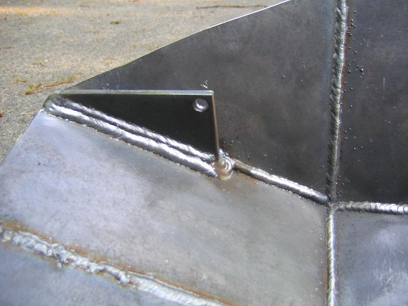 Close-up of a welded metal component with visible weld seams and a small drilled hole