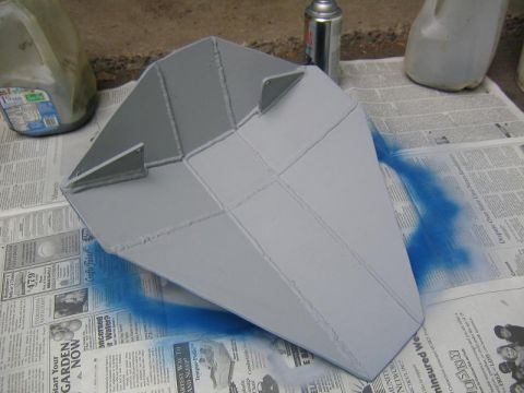 1978 Ford Bronco - A skid plate is being painted gray, with blue spray paint overspray visible on the newspaper beneath it.