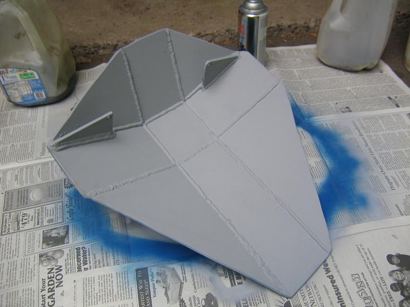 skid plate being painted gray with blue overspray on newspaper