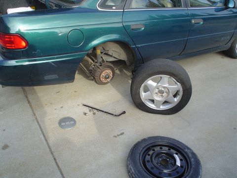 1993 Ford Taurus - A green 1993 Ford Taurus is shown with a flat tire removed, revealing the brake components and suspension.