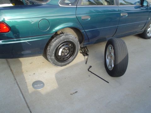 1993 Ford Taurus - Changing a flat tire on a 1993 Ford Taurus, with the spare and tools laid out.