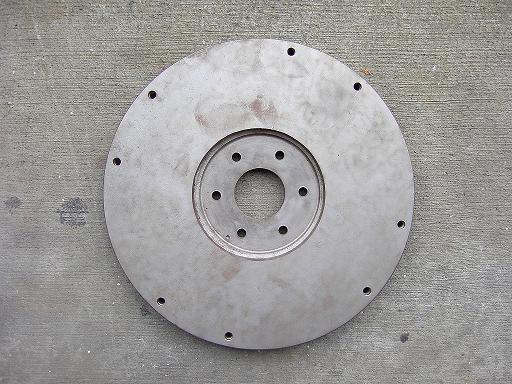 Bare steel flywheel adapter plate with outer and six-bolt hole patterns on concrete