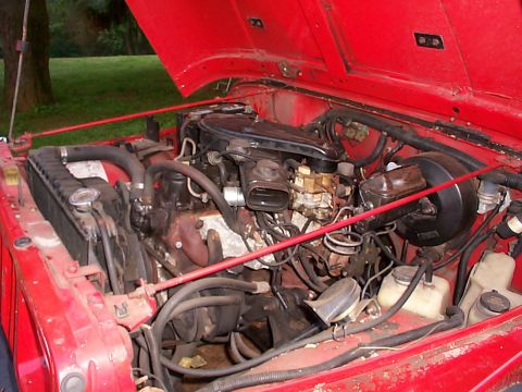 1989 Jeep YJ - The engine bay of a red 1989 Jeep YJ, showing the engine and various components with the hood raised.