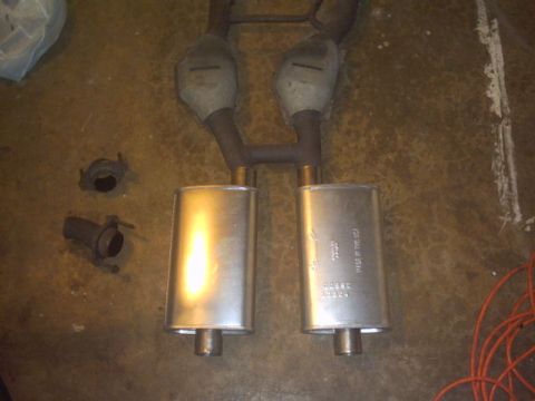 1991 Ford LTD Crown Victoria - A pair of exhaust mufflers and catalytic converters are laid out on the floor, showing part numbers for identification.