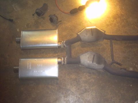 1991 Ford LTD Crown Victoria - Exhaust system components, including mufflers and catalytic converters, laid out on a concrete floor.