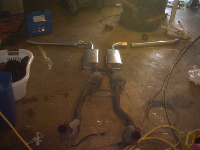 Car exhaust system with two mufflers and catalytic converters laid out on a garage floor