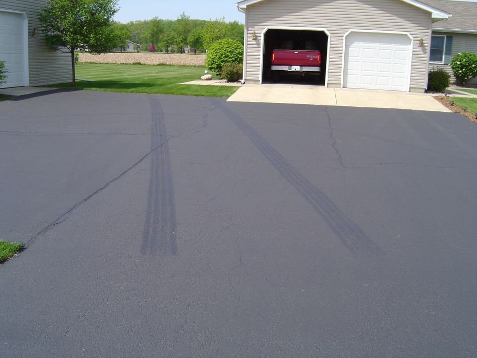Red pickup truck parked in an open garage bay. Tire marks are visible on the asphalt driveway