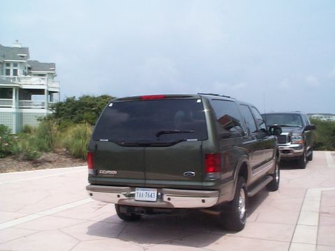 2001 Ford Excursion - Two large SUVs, a Ford Excursion and a pickup truck, are parked on a paved area near a house.