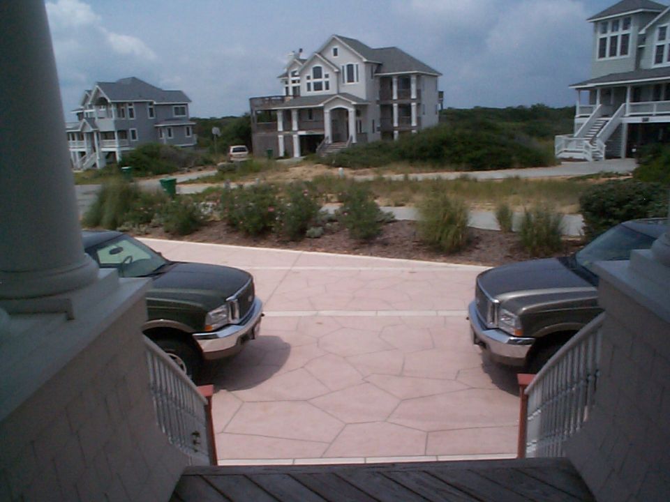 Two Ford Excursion SUVs parked front-facing on a patio with beach houses behind.