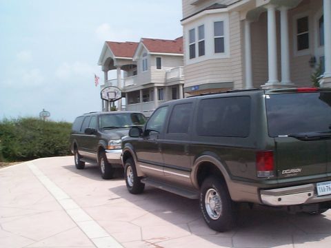 2001 Ford Excursion - Two Ford Excursions are parked in front of a beach house on a sunny day.