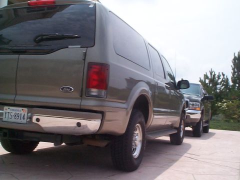2001 Ford Excursion - Two SUVs are parked on a paved surface, with trees and a cloudy sky in the background.