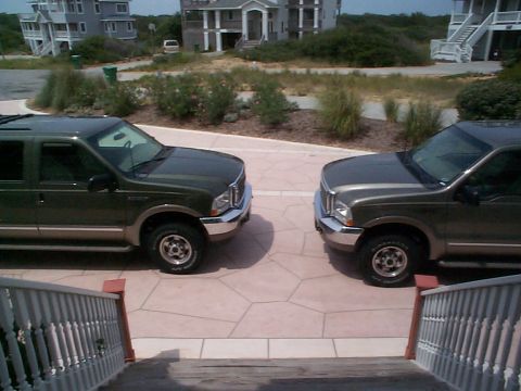 2001 Ford Excursion - Two Ford Excursions are parked on a paved driveway in front of houses.