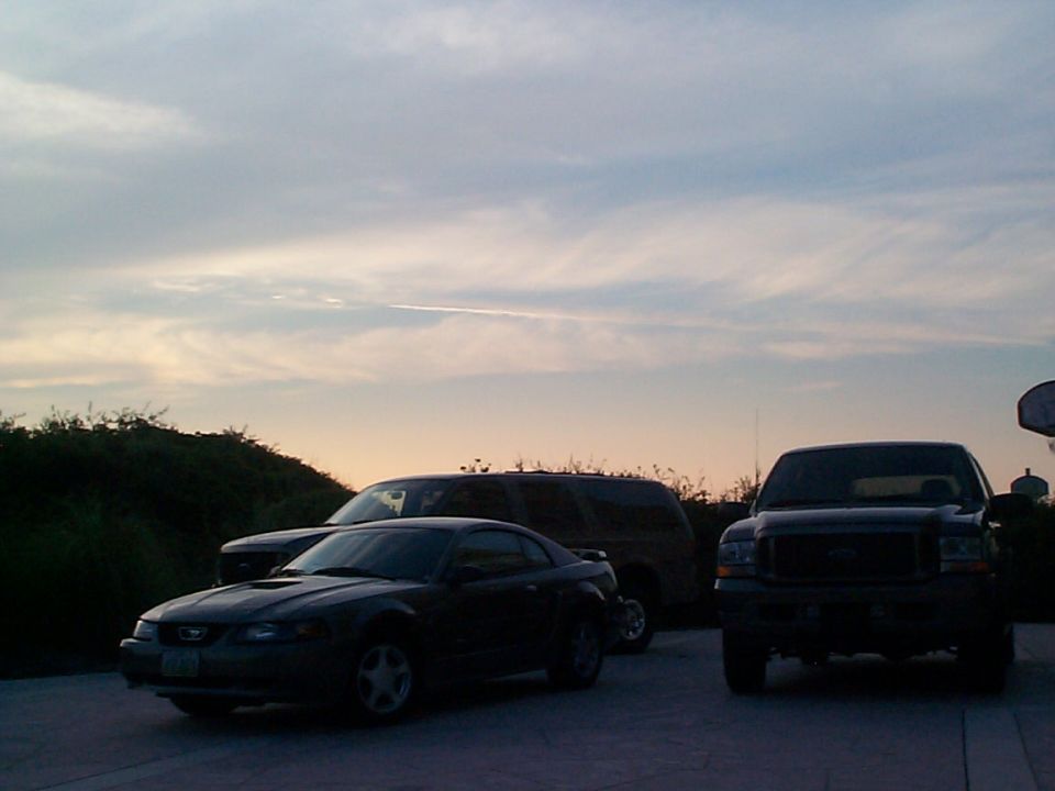 Dark coupe, SUV and large truck parked on pavement at dusk
