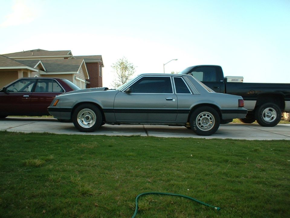 1982 Ford Mustang coupe parked next to a maroon sedan and a black pickup truck