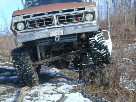 1976 Ford F-250 - Modified 1976 Ford F-250 navigating snowy, wooded area with large off-road tires.