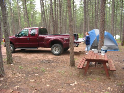 2000 Ford F-350 - A maroon Ford Super Duty pickup truck is parked at a campsite in a forest, with a tent and picnic table nearby.