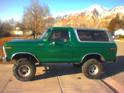 1979 Ford Bronco - This lifted green Ford Bronco is parked on a paved surface with mountains visible in the distance.