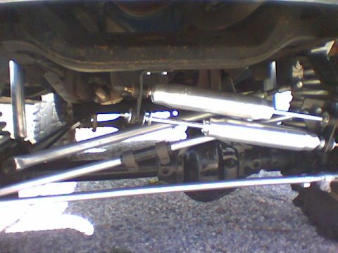 1979 Ford Bronco - View beneath the front of a lifted truck showing a solid front axle fitted with a dual steering stabilizer kit: two polished stabilizer sho…