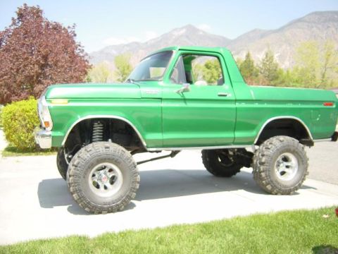 1979 Ford Bronco - Green first-generation-style Ford Bronco (late-1970s body) shown in side profile with a tall suspension lift, large off-road mud tires and…