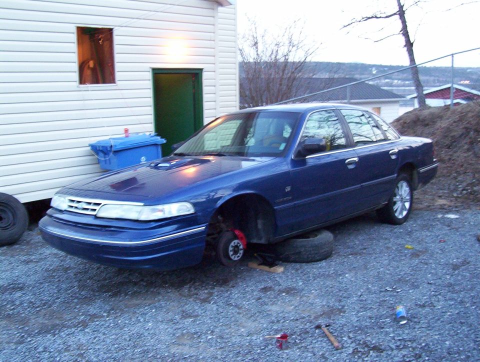Blue 1995 Ford Crown Victoria with front wheels removed, resting on tires