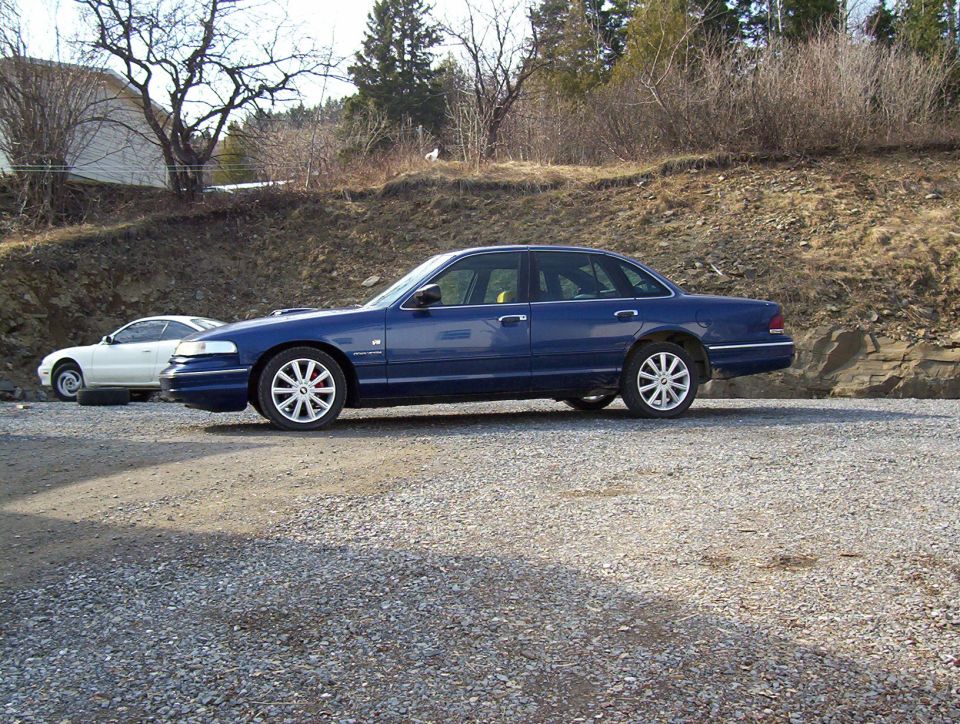 Blue 1995 Ford Crown Victoria sedan, side view. Another white car is parked behind it