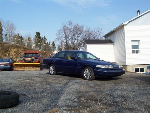 1995 Ford Crown Victoria - A 1995 Ford Crown Victoria is parked outside a building, with a snow plow truck visible behind it.