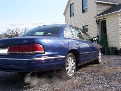 1995 Ford Crown Victoria - The rear of a blue 1995 Ford Crown Victoria sedan is visible, emitting smoke from the exhaust pipe.