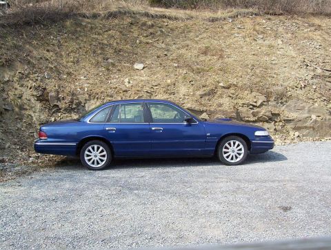 1995 Ford Crown Victoria - Blue 1995 Ford Crown Victoria parked on a gravel lot with a rocky hillside in the background.