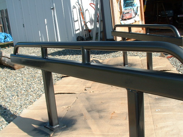 Pair of freshly painted black tube rock sliders drying on cardboard in a gravel shop yard