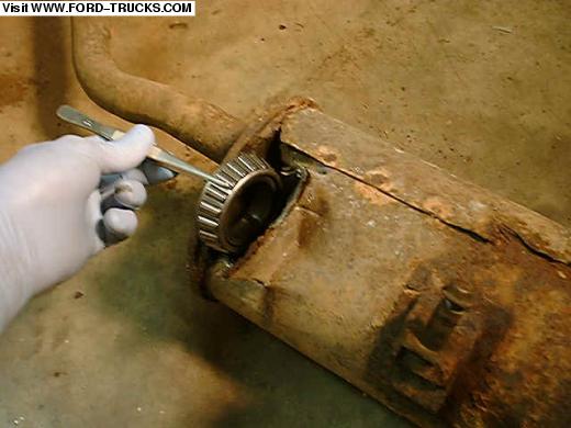 Gloved hand holding a roller bearing at the cut end of a rusty muffler, muffler-bearing joke