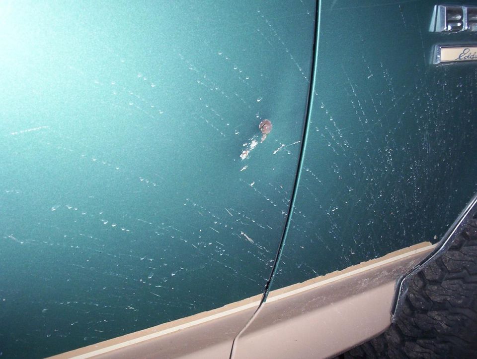 Close-up of scratched teal green vehicle door panel with paint damage near Eddie Bauer badge