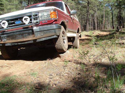 1990 Ford Bronco - A 1990 Ford Bronco navigates a wooded trail, kicking up dust on the path.