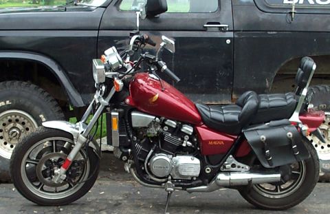 1986 Ford Bronco - Left-side profile of a maroon Honda Magna V4 cruiser with black leather saddlebag, stepped seat with sissy bar, and chrome mufflers, parked…