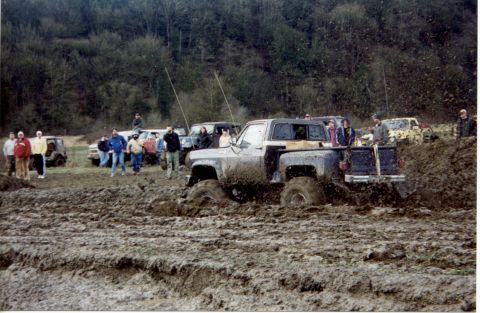 1990 Ford Bronco - Several trucks are stuck in deep mud during an off-road event.