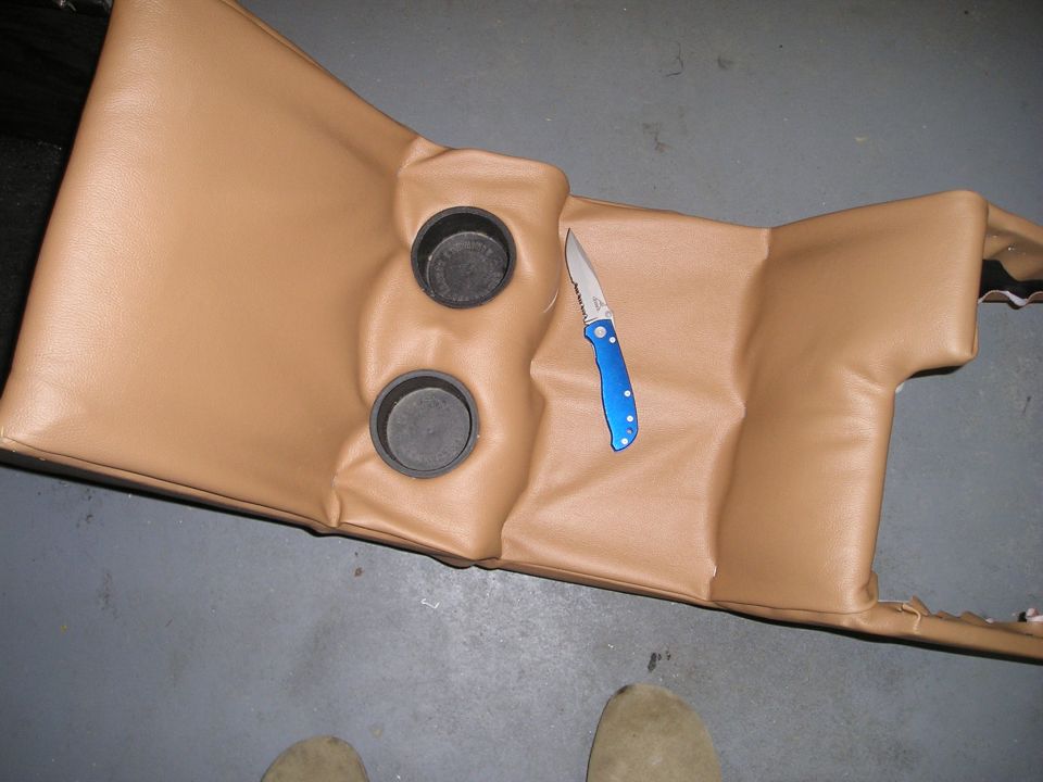 Tan vinyl recovered center console with two cupholders and a blue folding knife