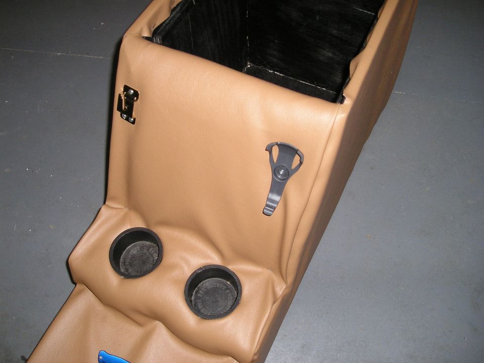 Custom tan vinyl center console with two cup holders and open black storage box on a concrete floor