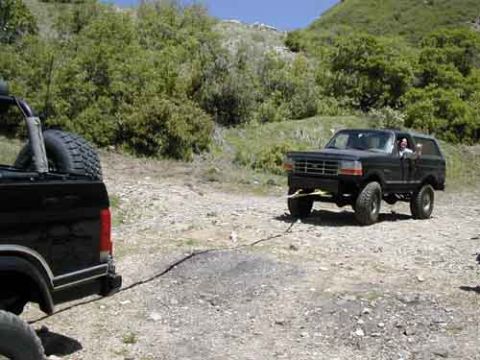 1994 Ford Bronco - A 1994 Ford Bronco is being towed by another vehicle on a dirt road with hills in the background.
