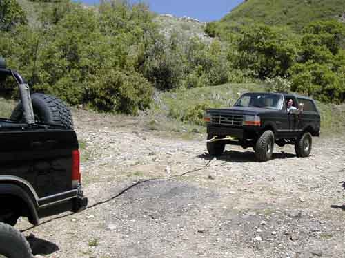 Black Ford Bronco being towed by another black vehicle off-road
