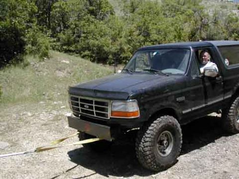 1994 Ford Bronco - A black Ford Bronco is parked on a gravelly surface with trees in the background.