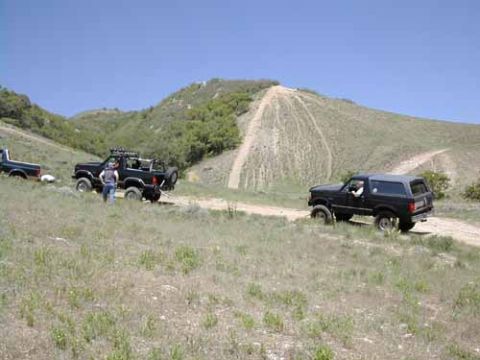1994 Ford Bronco - A black 1994 Ford Bronco navigates a dirt road in a scenic, hilly landscape.