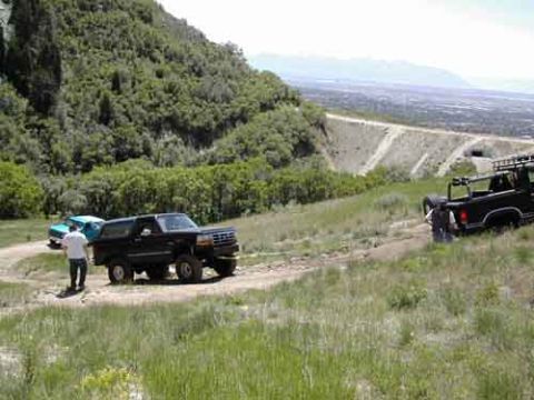 1994 Ford Bronco - Two trucks are parked on a dirt road on a grassy hill overlooking a valley.