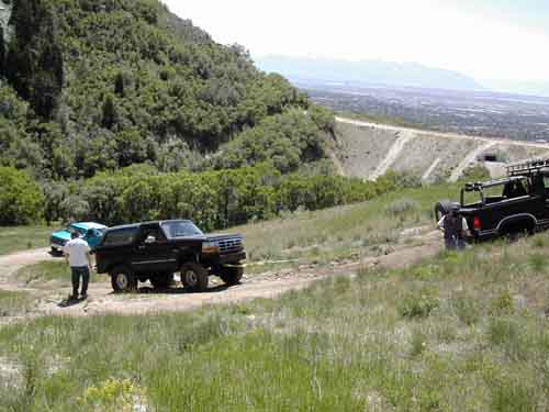Black Ford Bronco and black pickup truck on a dirt road with a valley in the background